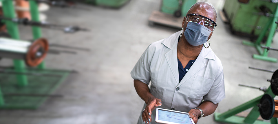 African senior employee with face mask using digital tablet in a factory