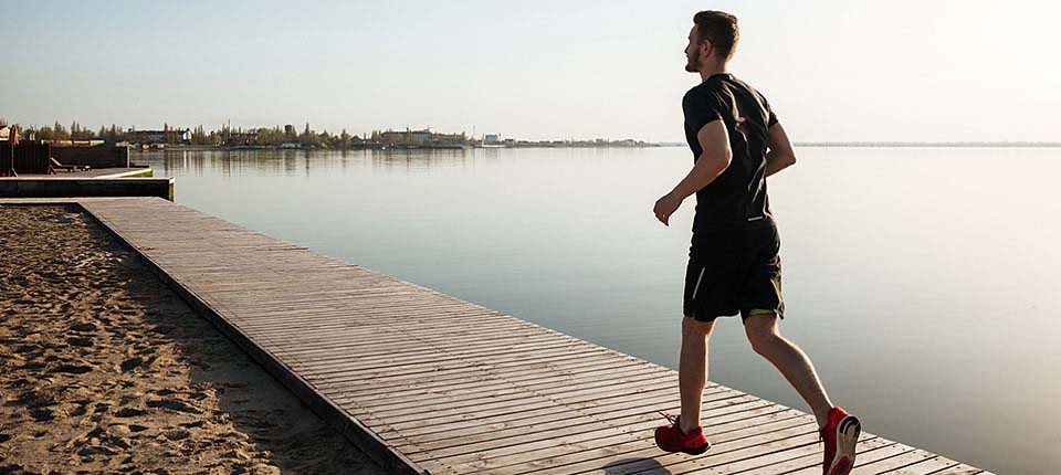 Back view full length portrait of a young sportsman running on the beach in the morning