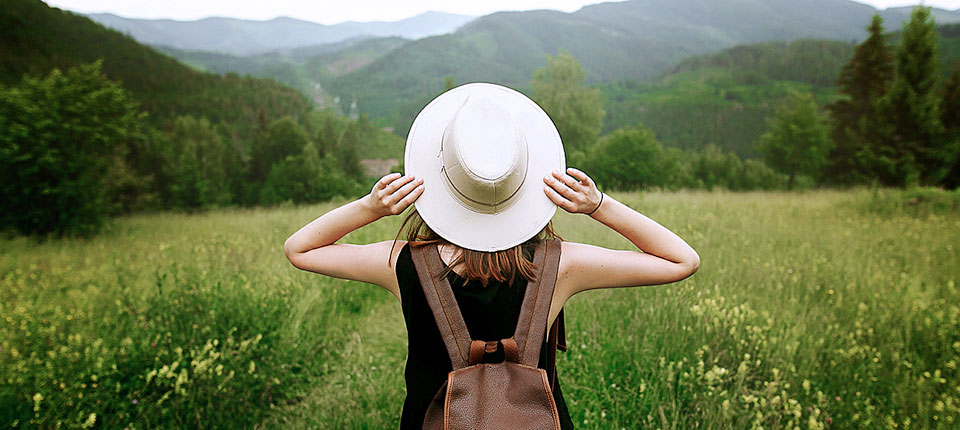 woman traveler with backpack holding hat and looking at amazing mountains and forest wanderlust travel concept space for text atmosperic epic moment