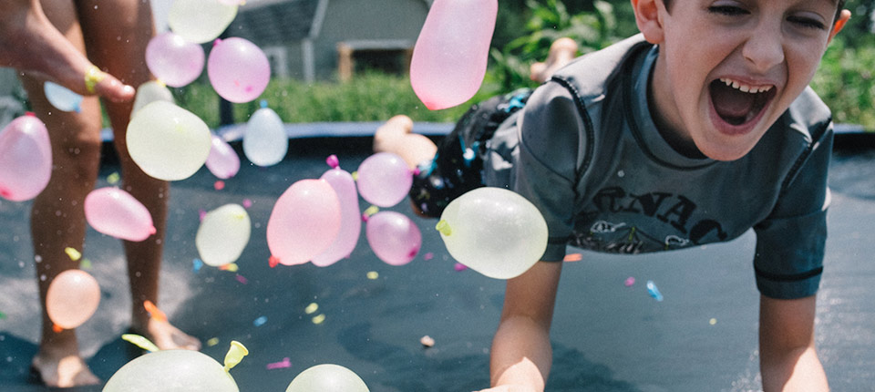 Kids jumping on a trampoline with water balloons on a hot summer day
