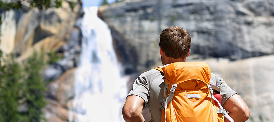 Hiker hiking with backpack looking at waterfall in Yosemite park in beautiful summer nature landscape. Portrait of male adult back standing outdoor.