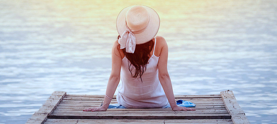 Woman in hat sitting at the end of dock and enjoying the sea view. Summer vacation concept.