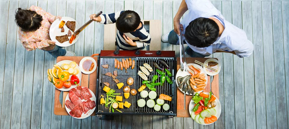 Family barbecuing proteins and vegetables on an outside grill.