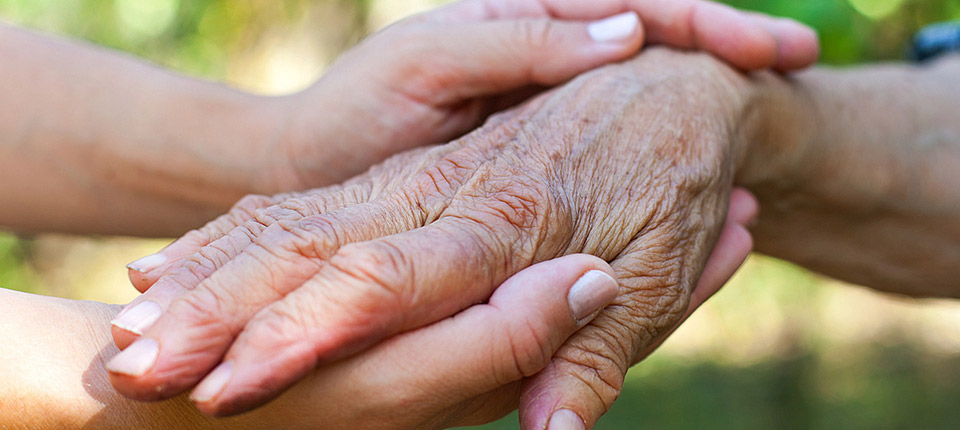Close up elderly female's shaking hand held by young carer's hands outdoor