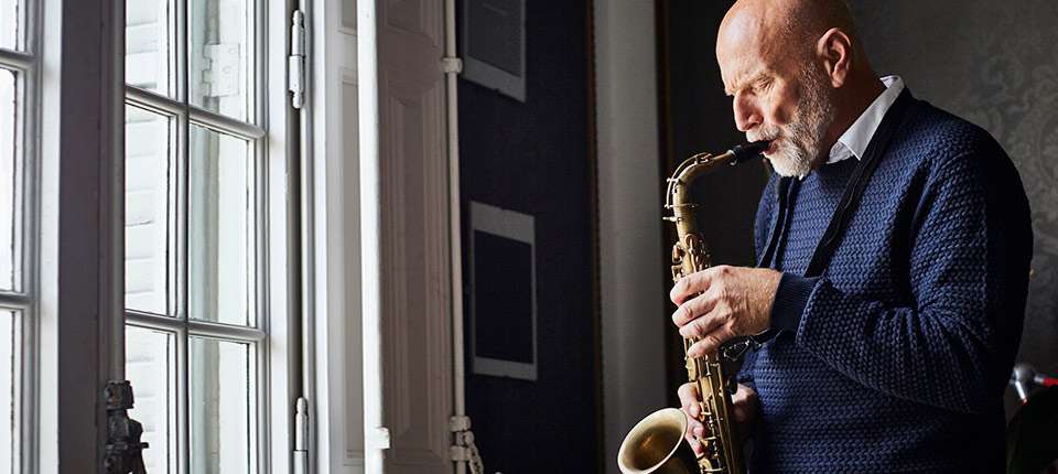 Senior man playing saxophone by window at home