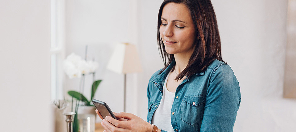 Casual woman in trendy denim relaxing at home with a mobile phone checking for messages with a quiet smile; Shutterstock ID 1008005938; PO: 123