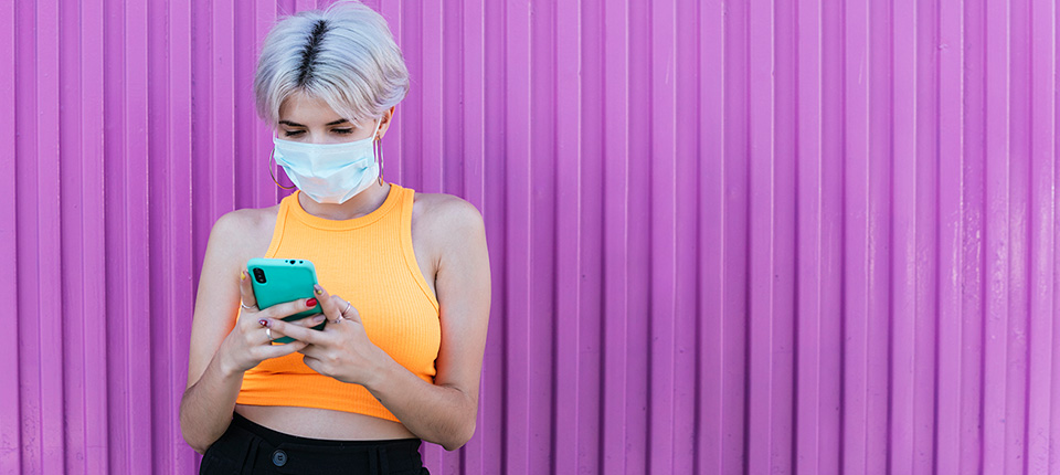 Portrait of woman with modern look and mask with mobile phone and purple urban background in Granada, Spain Woman young blonde "Gen Z" colorful mask covid19